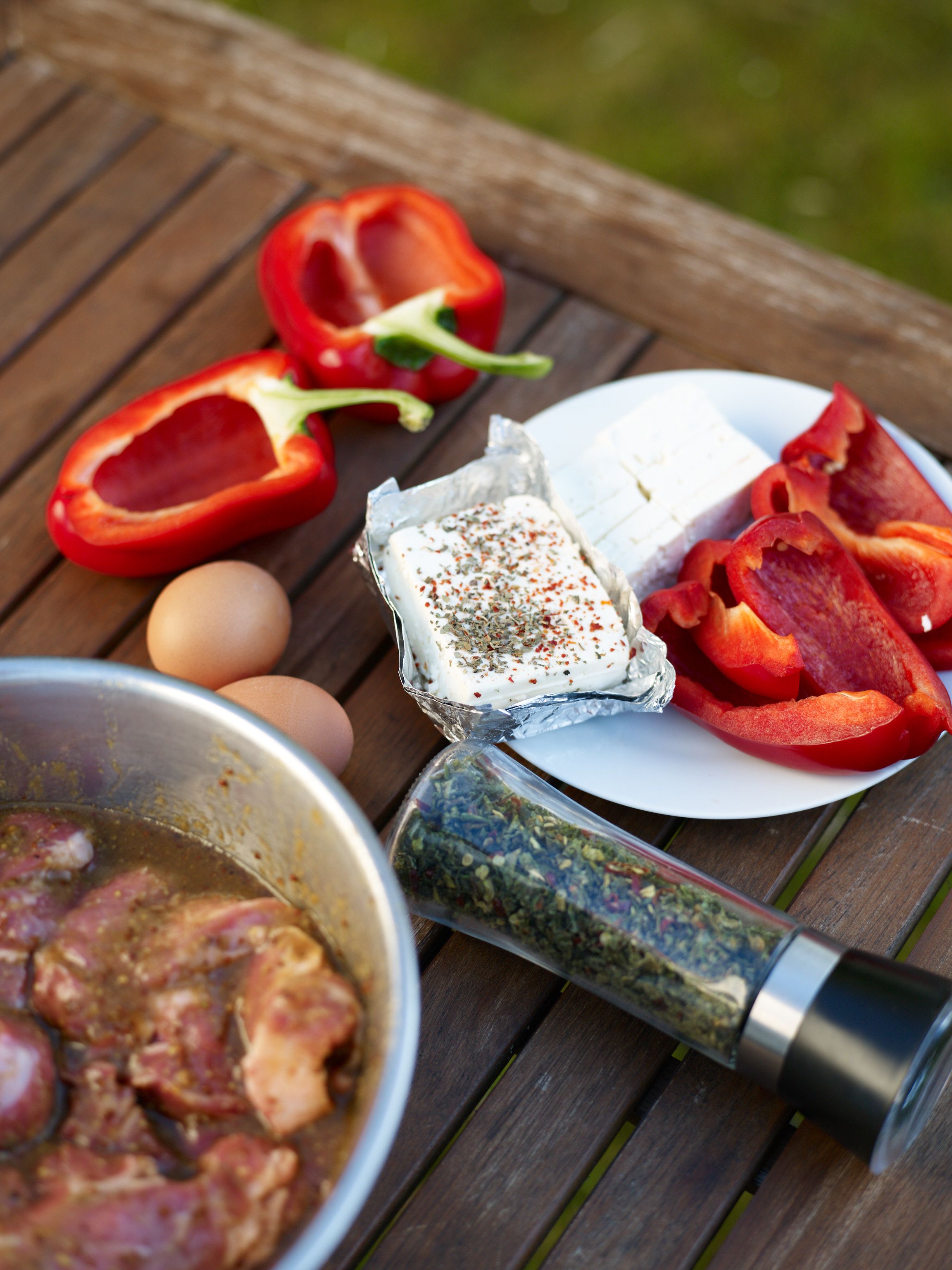 Barbecue ingredients: marinated pork, bell peppers, feta cheese, eggs as well as a shaker of chili flakes